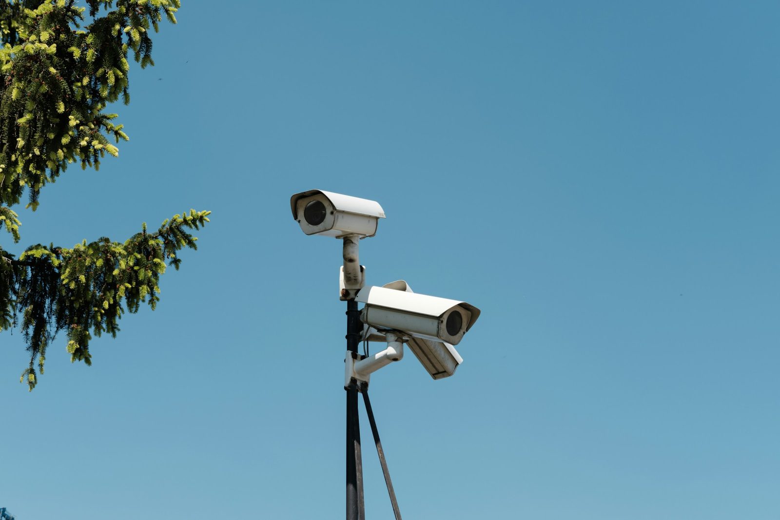 Two white surveillance cameras mounted on a pole against a clear sky